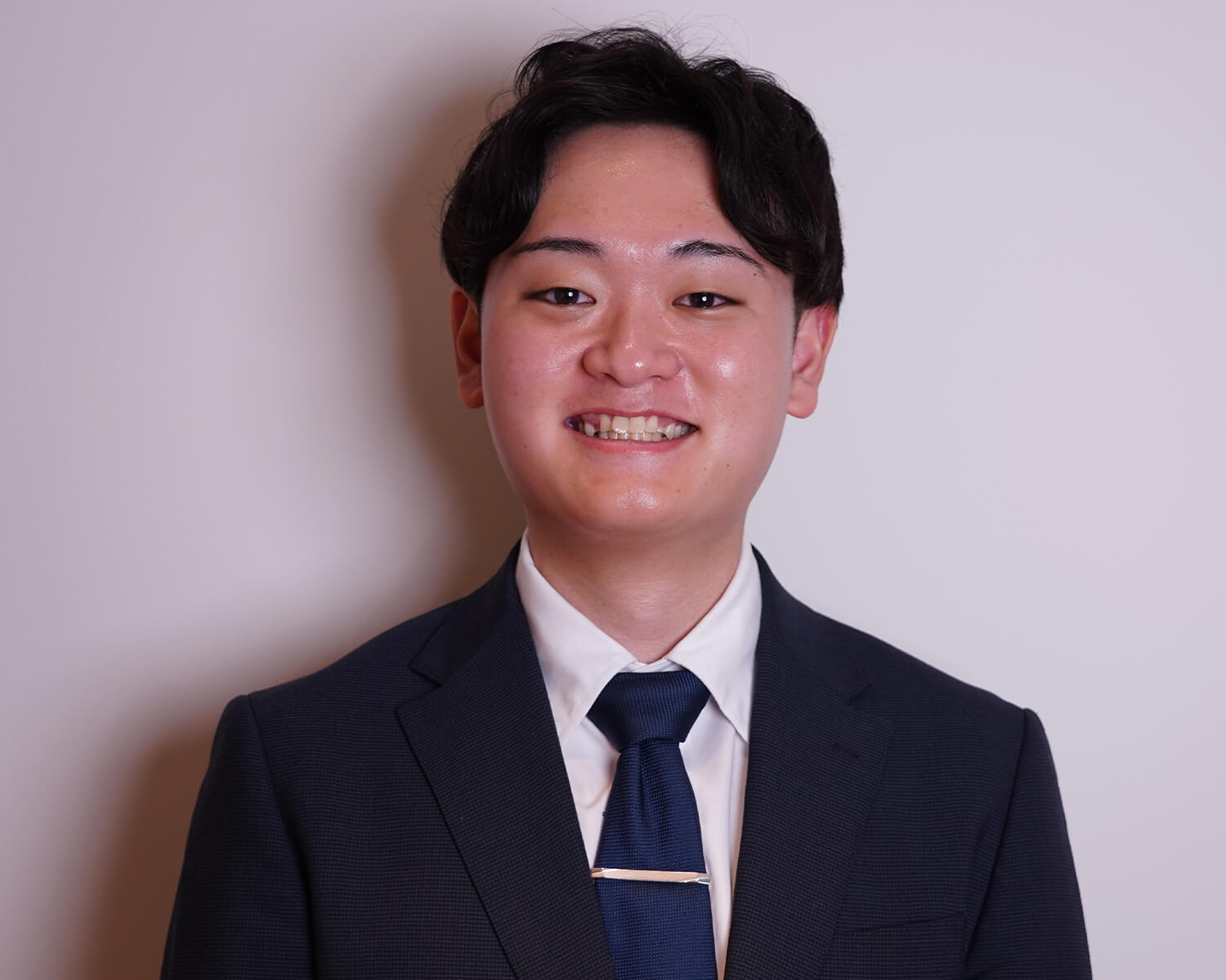 紺色のスーツとネクタイを着用し、白い背景の前で笑顔を見せる日本人男性のポートレート
