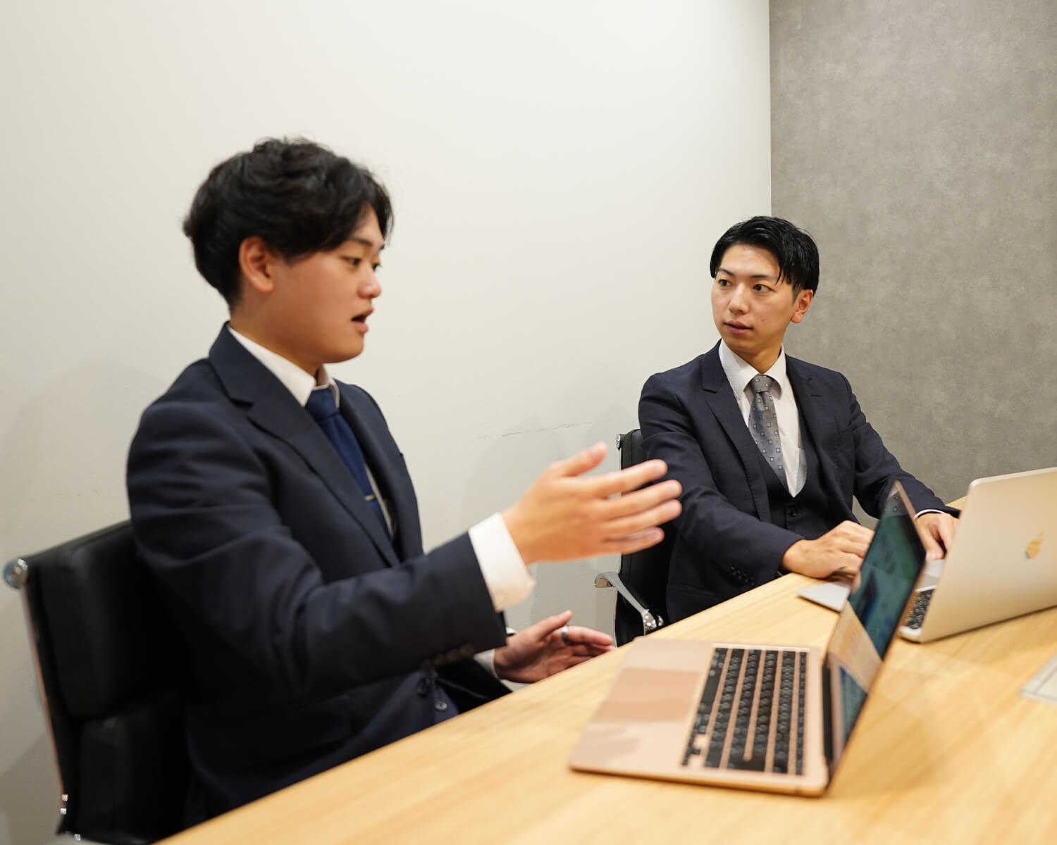 会議室のデスクでPCを前に、同僚とディスカッションを行うビジネスマンの様子