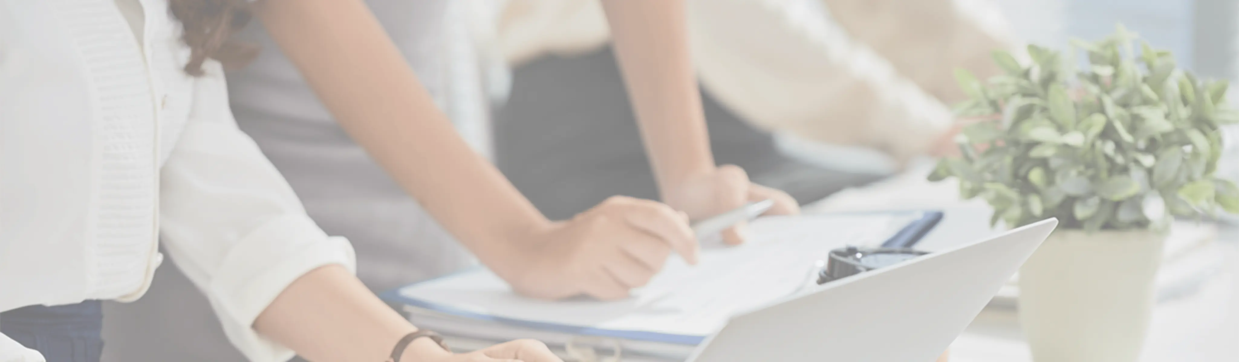 職場のデスクで、ラップトップや書類、メモを見ながら、女性従業員たちが共同作業をしている