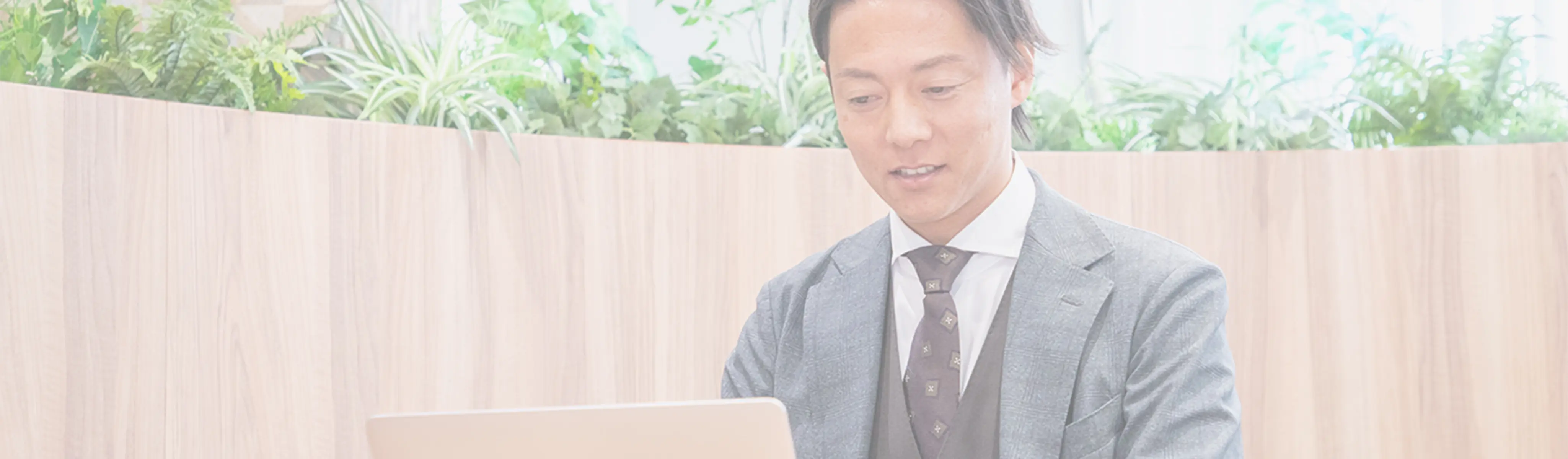 オフィスの共有スペースでパソコンに向かう、スーツ姿の日本人男性